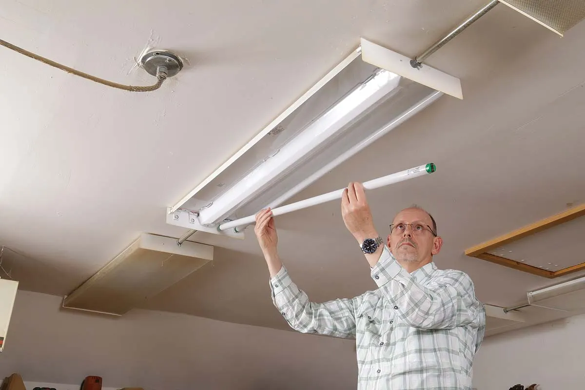 An electrician fitting a fluorescent tube into a ceiling-mounted batten light.