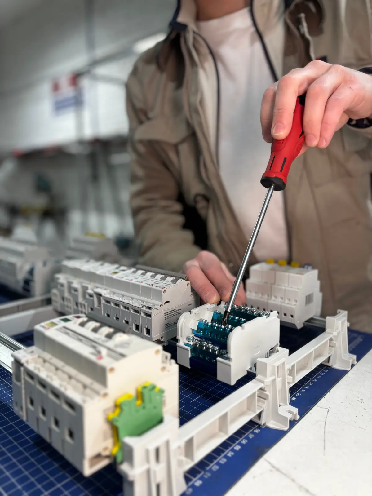 An electrician using a screwdriver to wire modular circuit breakers onto the DIN rail of a new consumer unit.