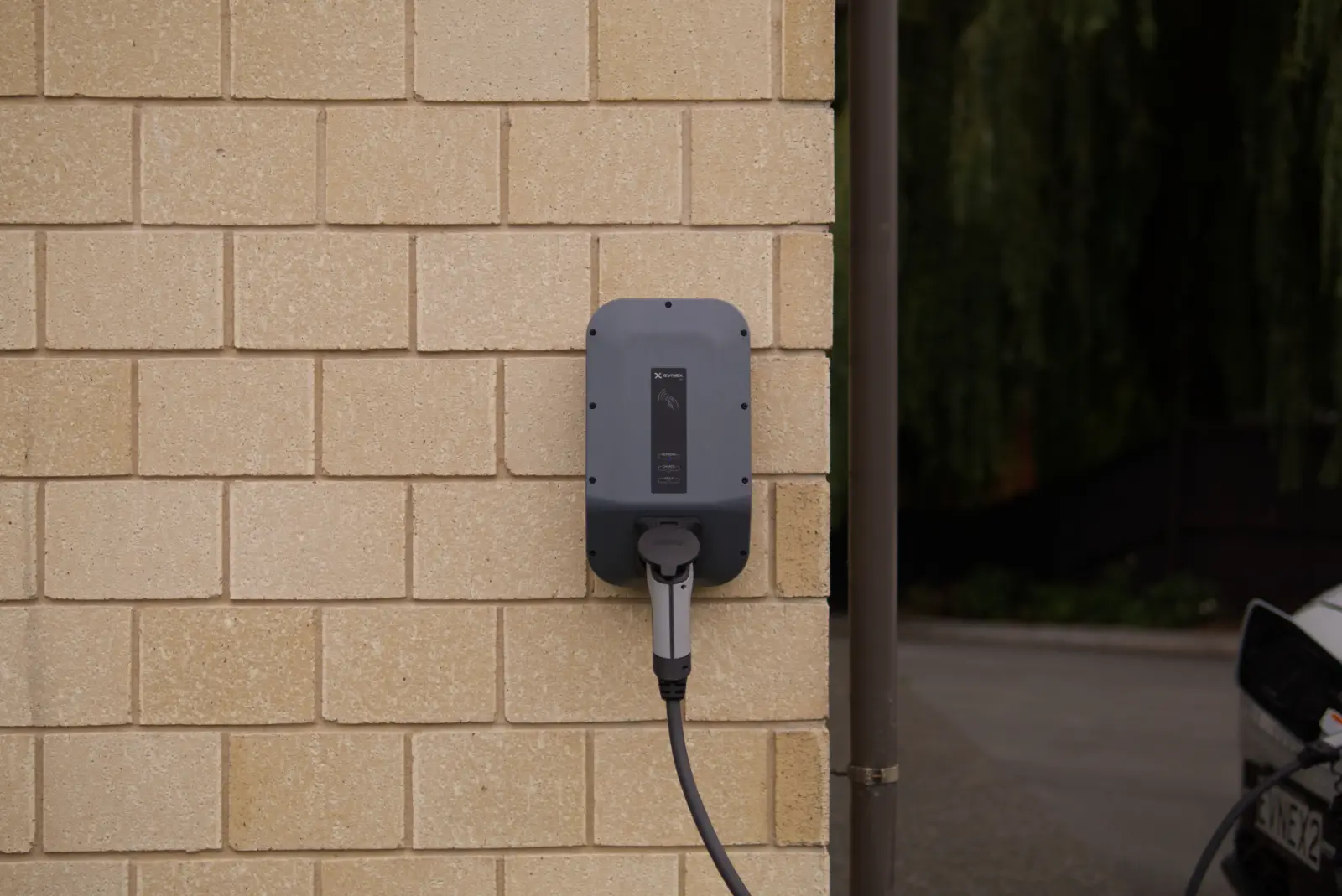 A wall-mounted electric vehicle charge point on the outside of a house, with the charging connector plugged in.